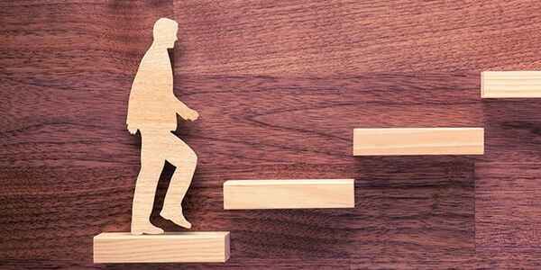 Wooden cutout of a person walking up a staircase made of wooden blocks, symbolising growth, progress, and personal or professional development.