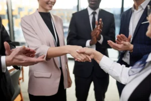 Two business people shaking hands while others clap