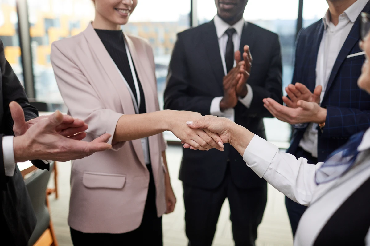 Two business people shaking hands while others clap