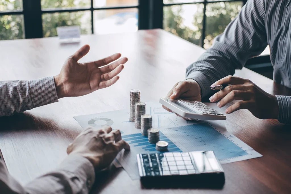 Two businesspeople discussing business valuation with charts and money on the conference table.